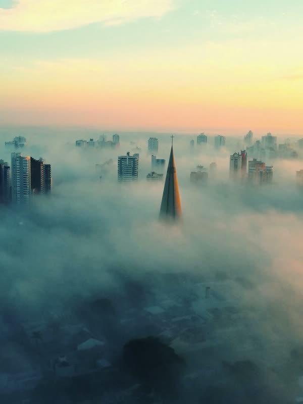Cidade emergindo de um mar de nuvens ao amanhecer